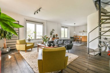 Çağdaş dairenin geniş odasındaki dinlenme odası ve mutfağın yakınındaki sandalyeli ve çiçekli masa.