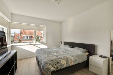 TV 'nin yanındaki yastıklarla aydınlık yatak odasındaki gardıroba karşı rahat bir yatak.