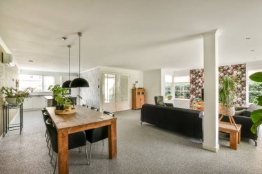 Çağdaş dairenin geniş odasındaki dinlenme odası ve mutfağın yakınındaki sandalyeli ve çiçekli masa.