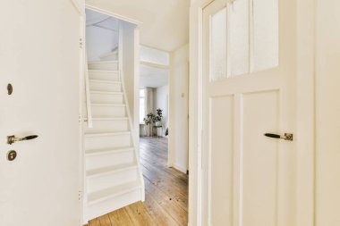 Minimalist iç tasarımı olan modern lüks dairenin ikinci katına çıkan ahşap merdivenli beyaz koridor.