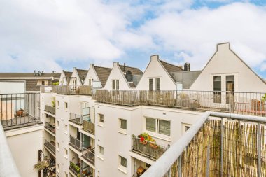 Metal parmaklıklı dar tuğla balkon, tahta sandalye ve camlı kapı mutfağa açılıyor.