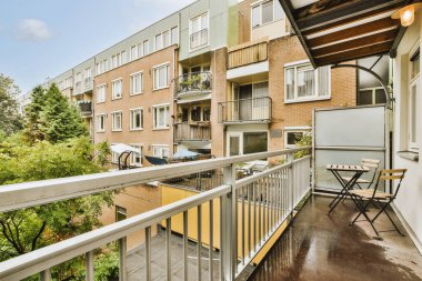 Metal parmaklıklı dar tuğla balkon, tahta sandalye ve camlı kapı mutfağa açılıyor.