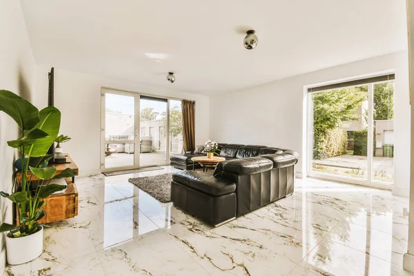 Stock image a living room with white marble flooring and black leather couches in the center of the room is an open patio