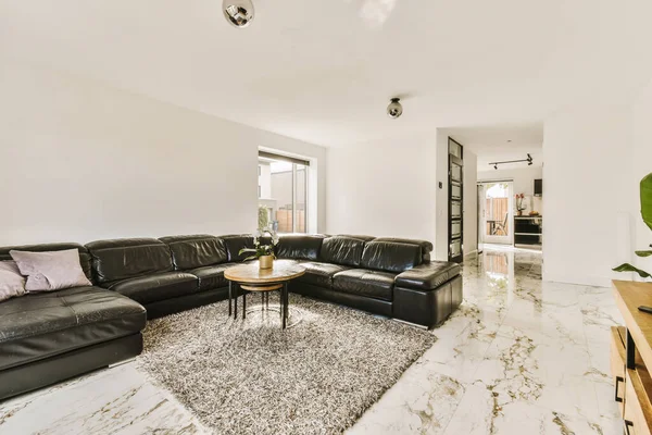 a living room with black leather couches and white marble flooring in the center of the room is a coffee table
