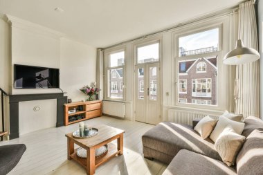 Masanın etrafında rahat kanepe ve koltukları olan, modern dairenin ikinci katına çıkan ahşap merdivenli bir oturma odası.