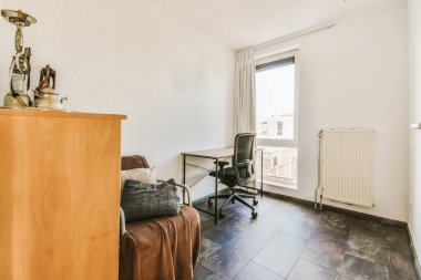 Masası, sandalyesi ve televizyonu olan bir oda. Dışarıdan bakan bir pencerenin önünde.