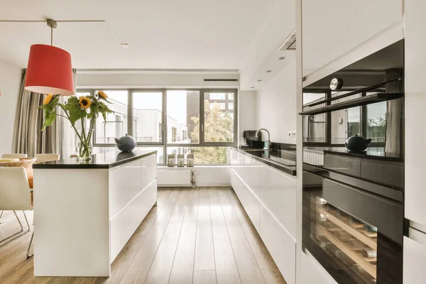 Stock image a modern kitchen with wood flooring and white cabinets in the center of the room is a red lamp hanging over the island