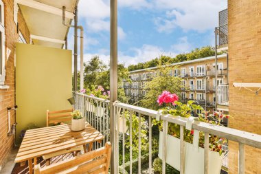 Ön tarafında ahşap banklar ve çiçekler olan bir balkon. Fotoğrafın sol tarafında pencereli bir alan.