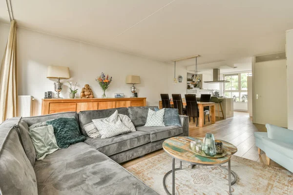 Çağdaş dairenin geniş odasındaki dinlenme odası ve mutfağın yakınındaki sandalyeli ve çiçekli masa.