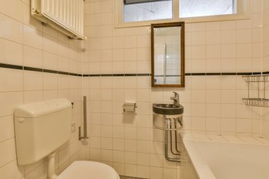 Duvarlarında beyaz fayanslar ve siyah süslemeler olan bir banyo ve odanın köşesinde bir tuvalet.