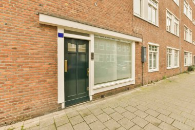 Sağ tarafında mavi kapısı ve penceresi olan tuğlalı bir bina. Önünde boş bir kaldırım var.