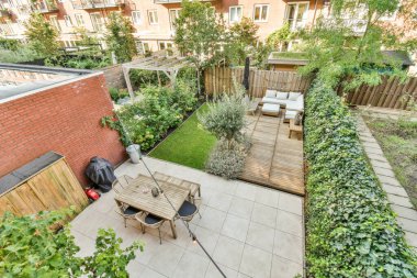 Tuğla bir binanın önüne kurulmuş küçük bir arka bahçe ve bazı bitkiler ve açık hava mobilyaları.