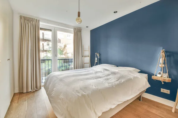a bedroom with blue walls and white bedding in the middle of the room, there is a wooden floor