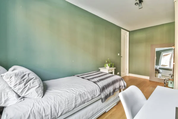 a bedroom with a bed, desk and mirror on the wall in front of the room is green painted walls