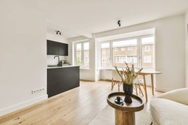 Odanın ortasında beyaz duvarları ve ahşap döşemeleri olan bir oturma odası açık bir mutfak alanıdır.