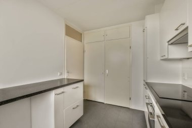 Buzdolabının önünde beyaz dolapları ve siyah tezgahları olan boş bir mutfak var.