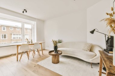 Oturma odası, bir kanepe, masa ve pencereyle apartman pencerelerinin önündeki sokağa bakıyor.