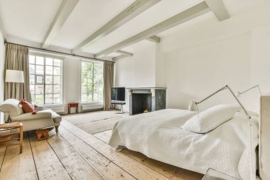 Geniş yatak odasındaki televizyon ve şöminenin yanındaki rahat yatağı ve kanepesi olan modern bir yatak.