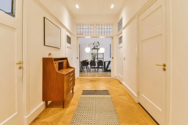 a long hallway with hardwood flooring and white trim on the walls, there is a small desk in the corner
