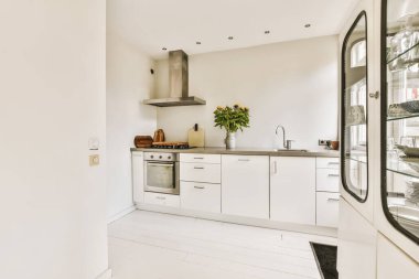 Duvarında beyaz dolaplar ve siyah tezgahlar olan açık bir plan alanı olan bir mutfak.