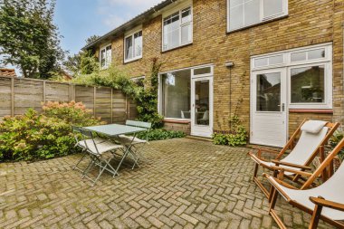 Bahçenin ortasında tuğla duvarlarla çevrili sandalye ve masa olan bir avlu.