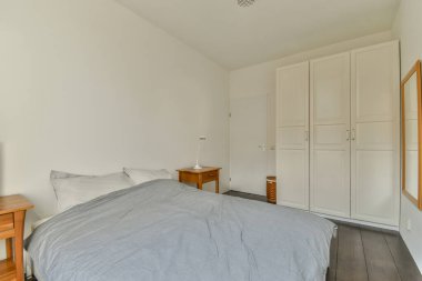 Rahat yataklı, yumuşak yastıklı, komodinin yanında ve geniş yatak odasındaki gardırobu olan modern bir yatak.