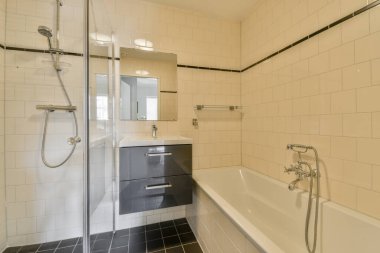 Modern banyo. Dikdörtgen aynası ve temiz lavaboları modern banyo odasındaki duş kabininin yanındaki beyaz fayanslı duvara bağlı.