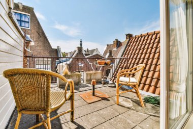 Dar tuğlalı balkon, metal parmaklıklar, tahta sandalye ve kapı.