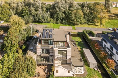 Önünde ağaçlar ve çalılar olan bir evin havadan görünüşü yukarıdan çekiliyor, aşağıya bakıyor.