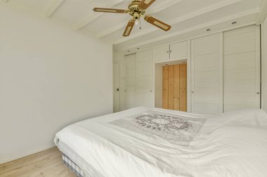 Comfortable bed with white bedclothes and bedside table placed near window in light bedroom at home