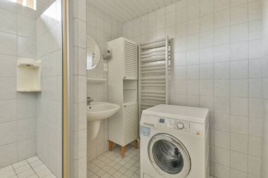 Çağdaş dairenin küçük fayanslı banyosunda lavabo ve duş arasında yer alan tuvalet.