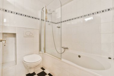 Yerde siyah beyaz fayanslar, duş kabini ve odanın köşesinde tuvalet olan beyaz bir banyo.