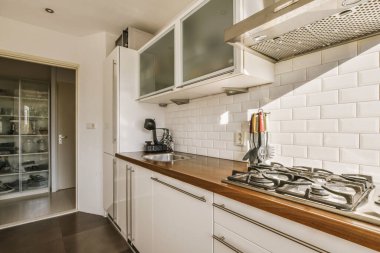 Ocağın, fırının ve bulaşık makinesinin önündeki tezgahların üzerinde beyaz fayanslar ve ahşap tezgahlı bir mutfak.