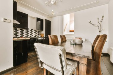 Beyaz duvarları, ahşap döşemeleri ve siyah dolapları olan bir odada yemek masası ve sandalyeler.