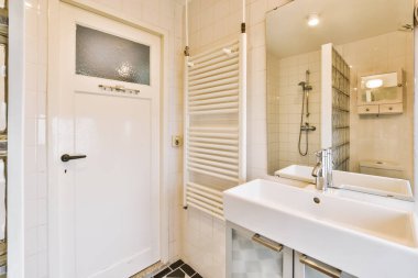 Lavabosu, aynası ve havlusu olan bir banyo. Odanın kapısının önündeki duvarda.