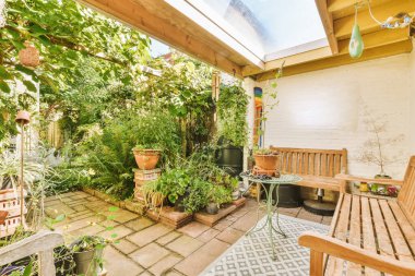 Sarıya boyanmış beyaz tuğla bir duvarın önünde yerde bir sürü bitki ve çömlek olan bir teras.