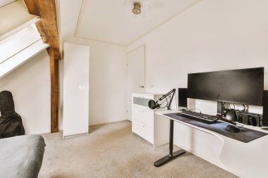 Modern apartmandaki hafif iş yerinde bilgisayar monitörleri ve beyaz tahtanın olduğu masanın yanına konforlu sandalye