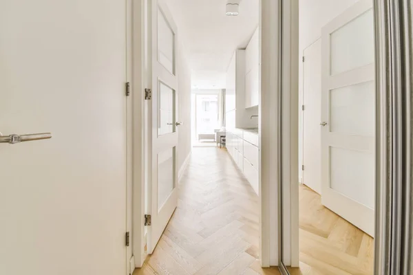 a long hallway with white walls and wood flooring on either side by side, leading to an open door