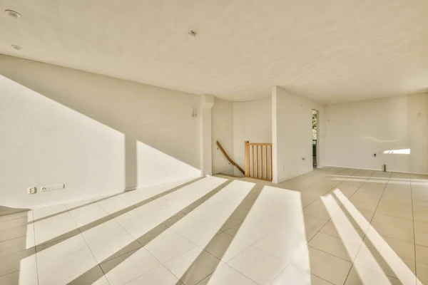 an empty living room with white tile flooring and wooden staircase leading up to the second floor in this house