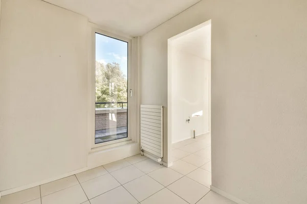 an empty room with white walls and tile floor, looking out to the garden outside from the living room door