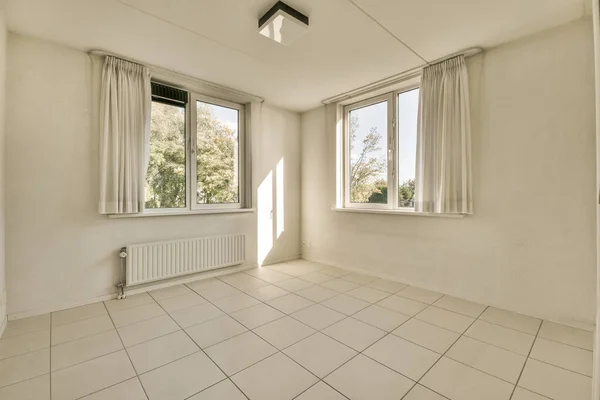 an empty room with white tile flooring and large windows looking out onto the trees in the distance from the window
