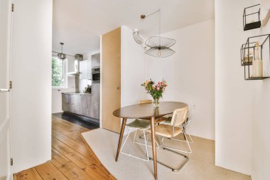 Beyaz duvarları, ahşap zemini ve mutfağa açılan kapısı olan bir odada yemek masası ve sandalyeler.