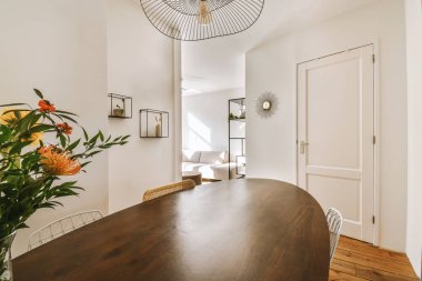 Masasında çiçekler olan bir yemek odası ve odanın arka duvarındaki açık bir kapı beyazdır.