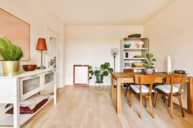 Beyaz duvarları, ahşap döşemeleri ve duvarları açık renkli mobilyaları olan bir odada yemek masası ve sandalyeler.