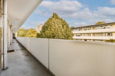 Arka planda ağaçlar ve binalar olan bir dış alan. Balkondan sokağa bakıyor.