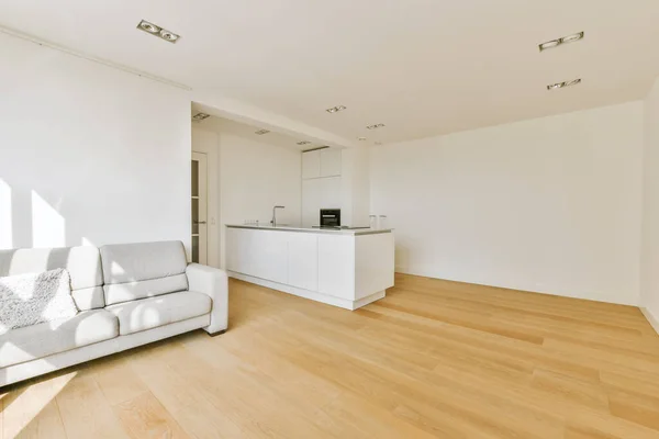 a living room with hardwood flooring and white walls, including a large kitchen island in the area is well lit