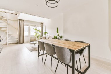 Beyaz duvarları ve ahşap döşemeleri olan bir yemek odası. Ortasında gri sandalyelerle çevrili ahşap bir masa.