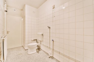 Duvarlarında beyaz fayanslar olan bir banyo ve duş kabini kapısının yanında bir tuvalet.