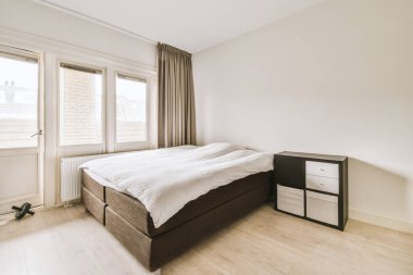 Beyaz duvarları ve ahşap döşemeleri olan bir yatak odası. Odanın ortasında bir yatak da açık bir pencere.