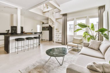 Odanın ortasında kanepeleri, sandalyeleri ve kahve masası olan bir oturma odası açık bir mutfak.